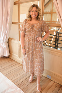 Model wearing a mocha floral midi dress featuring a front tie, smocked waist, side pockets, and a comfortable fully lined design, perfect for any occasion.